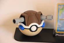 The Blastoise Pokéball up close: cream with the brown shell, two grey water cannons and blue arms.