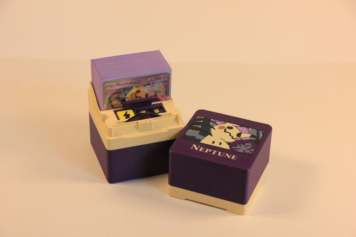 standard_pokemon|Purple and cream Pokémon Standard deck box open with a Mimikyu ex deck and damage-counter dice, beside a closed box with a Mimikyu lid and Neptune nameplate