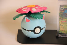 The Venusaur Pokéball up close: light blue with the pink flower, green leaves, pink-tipped ears and small fangs.